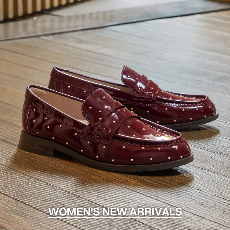 Pair of burgundy patent leather women's loafers with decorative gold studs displayed on a wood floor. Text reads &ldquo;Women's New Arrivals.&rdquo;